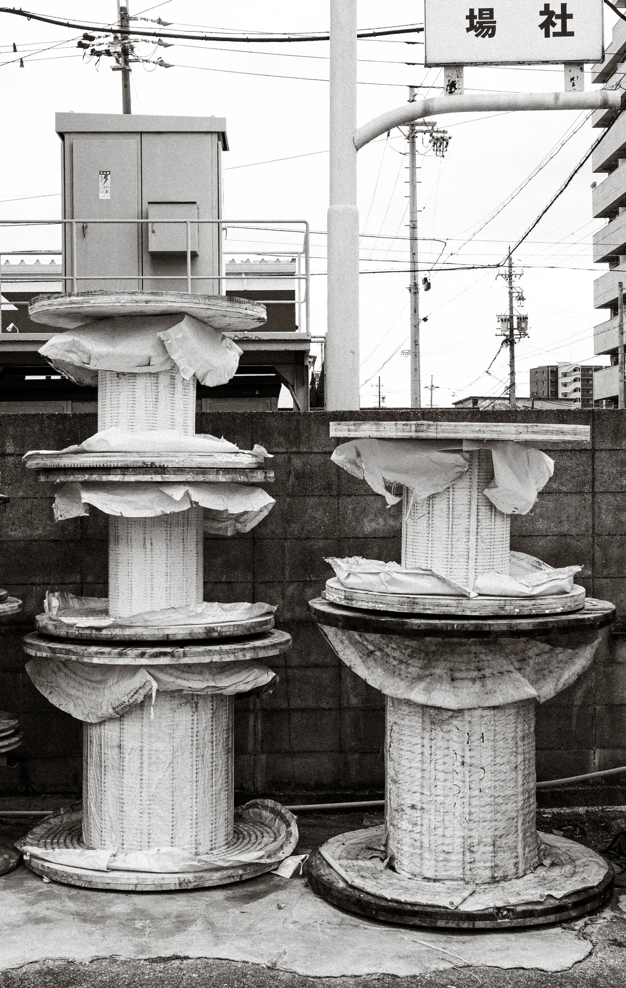 Large wooden cable reels stand stacked beside a block wall, with torn wrapping around their centers.