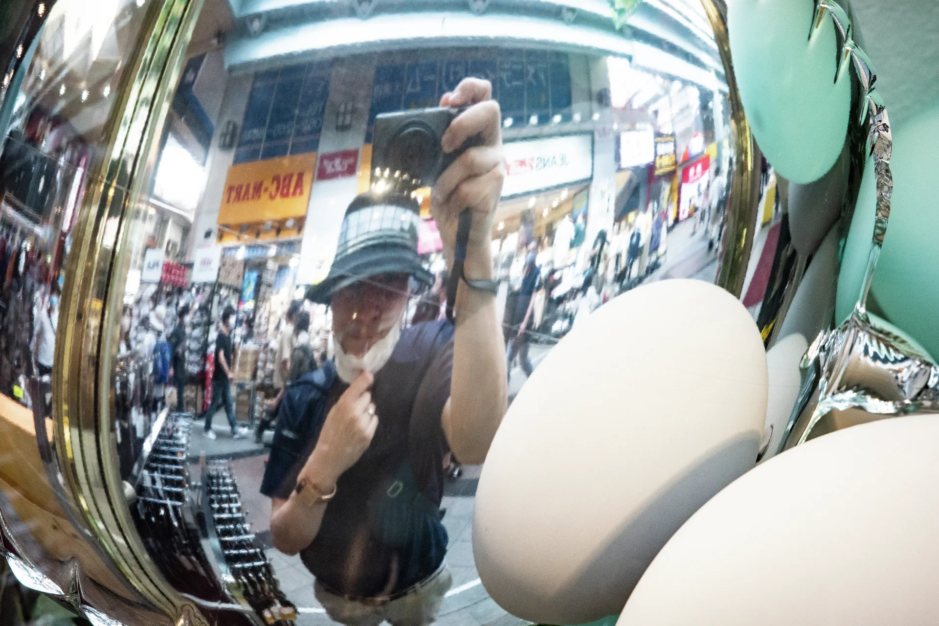 A curved reflective surface distorts a person holding a camera beside pale oval forms.