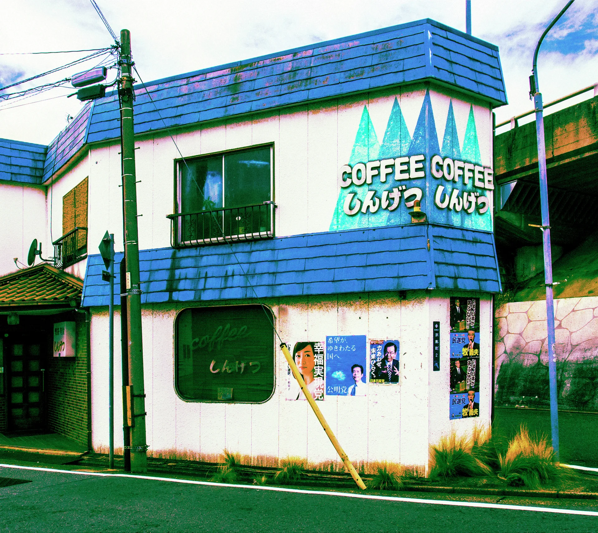 A white coffee shop building has blue trim, triangular painted patterns and posters near its corner entrance.