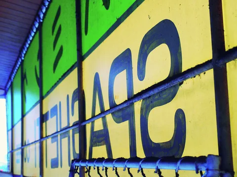 Large dark letters stretch across yellow and green window panels behind horizontal metal bars.