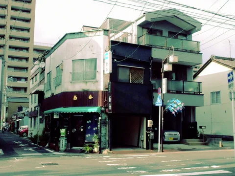 A weathered corner shop with a green awning stands beside a dark building with stacked balconies.