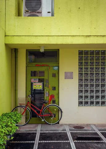 A red bicycle leans outside a recessed entrance in a yellow building beside a glass-block window.