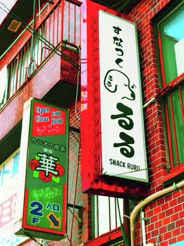 A white vertical Snack Ruru sign projects from red brick beside a narrow green Japanese sign.
