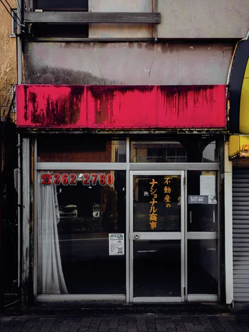 A stained bright pink fascia hangs above dark glass storefront doors with small Japanese lettering.