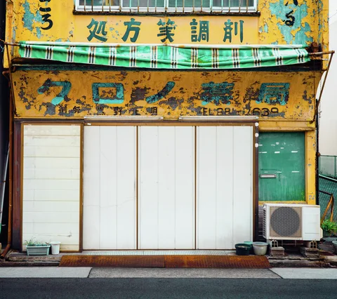 Peeling yellow signs and a green-striped awning hang above closed white storefront panels.