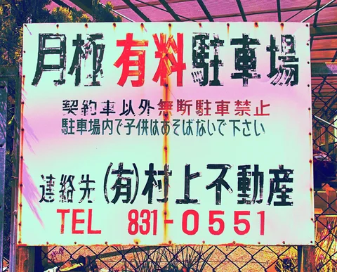 Black and red Japanese parking information covers a large pale sign with rusty streaks.