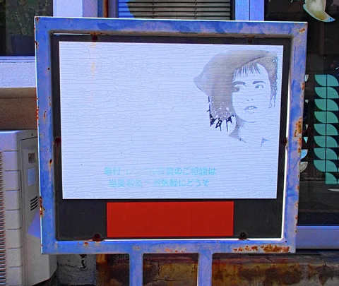 A faded portrait advertisement fills a freestanding display with a rusted blue frame and red lower panel.