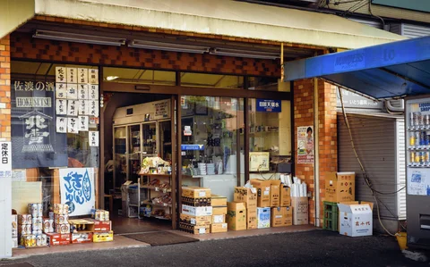 Cardboard boxes and drink containers line a shop entrance beneath a weathered canopy.