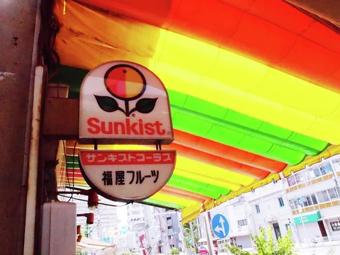 A Sunkist fruit sign hangs beneath a translucent awning striped orange, yellow, and green.
