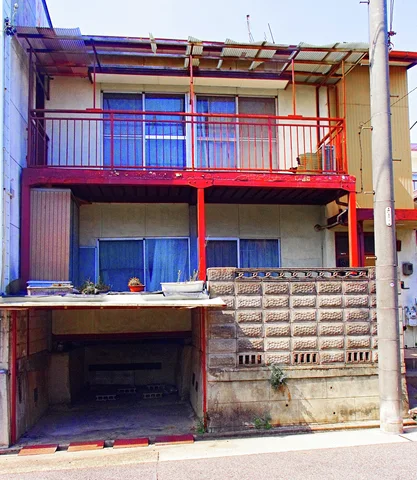 Red balcony supports and railings contrast with pale siding above a recessed garage and concrete block wall.