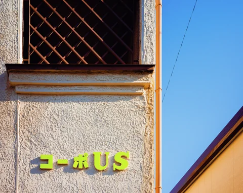Lime-green raised lettering marks a textured cream facade beneath a diagonal wooden window grille.