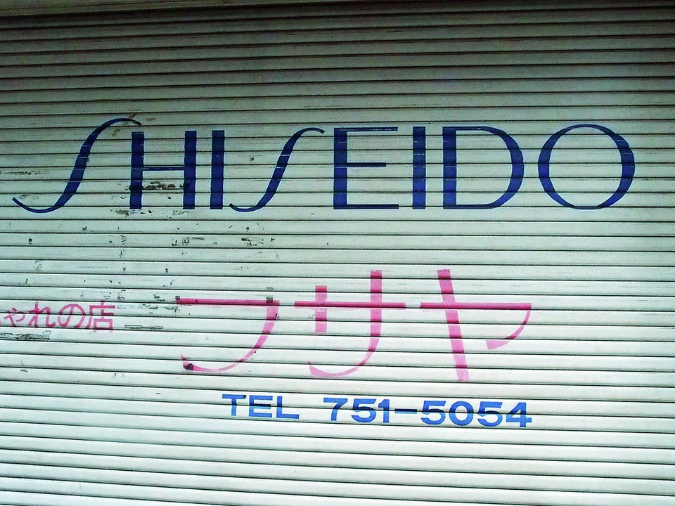 Blue SHISEIDO lettering and pink Japanese characters cover a closed pale green metal shutter.