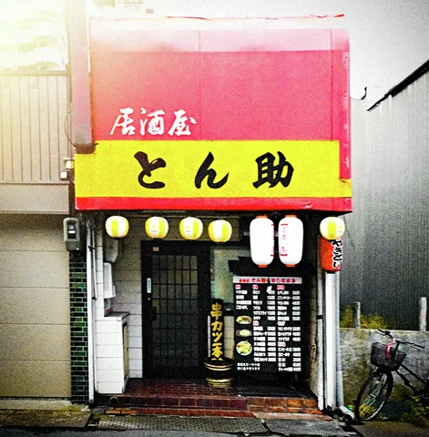 Yellow lettering and hanging lanterns mark a narrow restaurant entrance beneath a red facade.