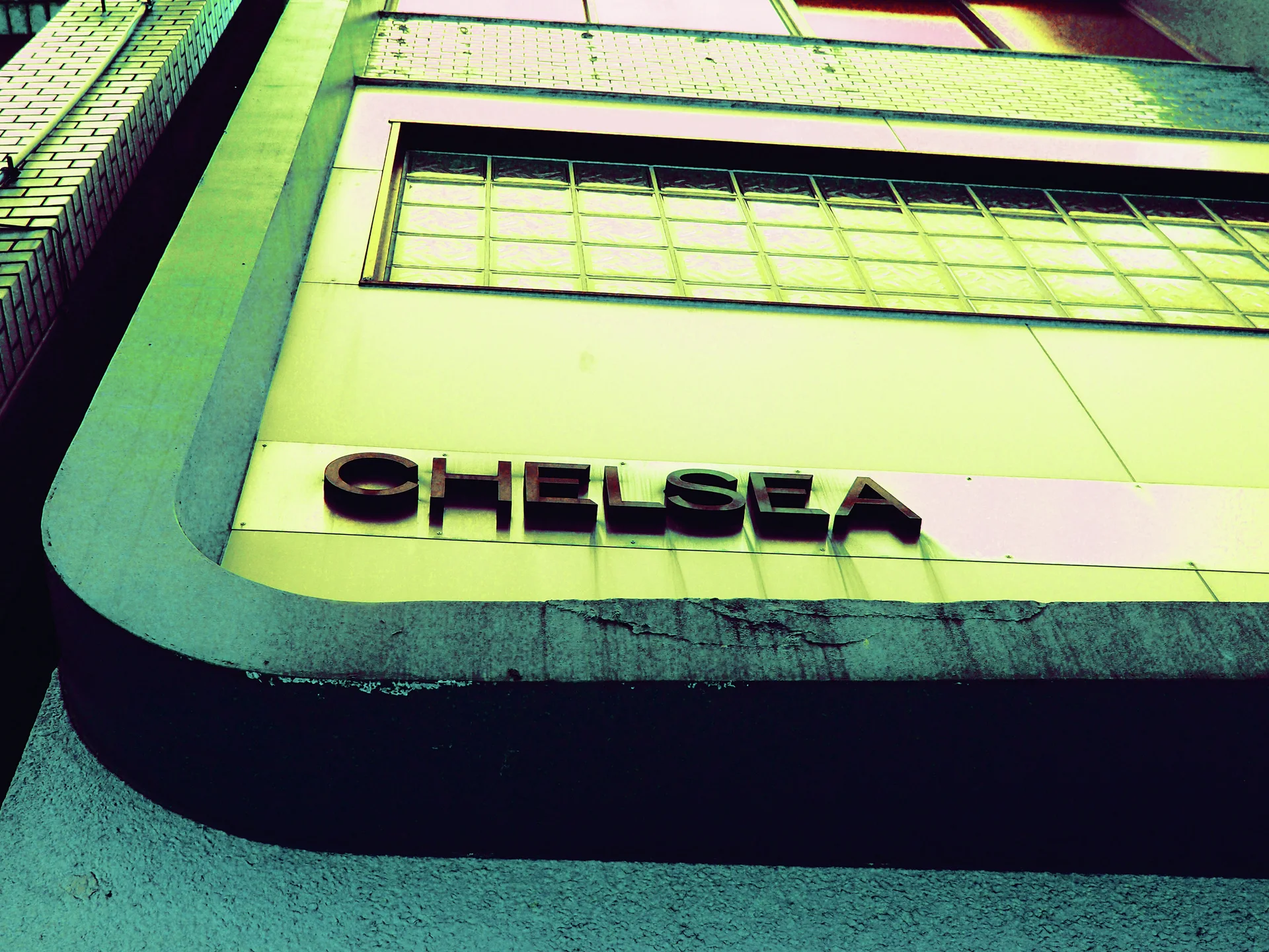 Raised dark CHELSEA lettering sits beneath horizontal windows on a pale green building facade.