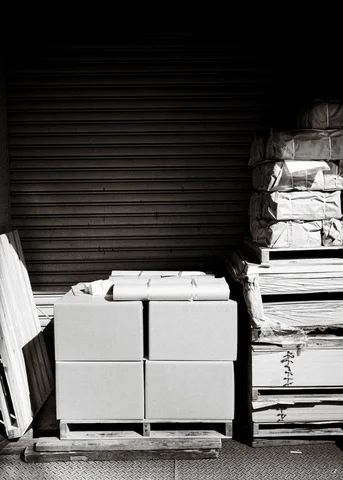 Stacked concrete blocks and wooden pallets stand before a dark closed shutter in black and white.