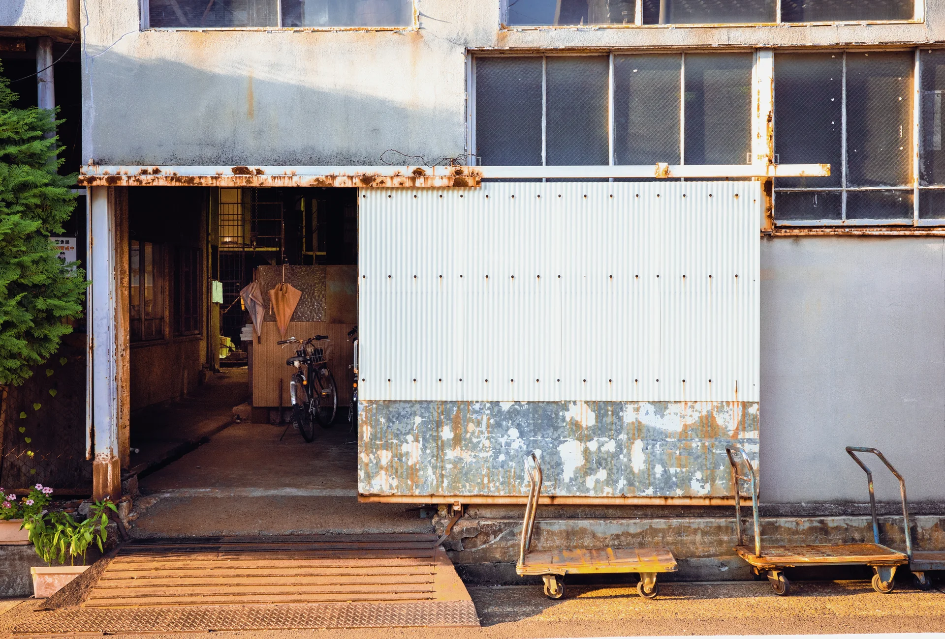 Rust stains mark a pale industrial facade with an open doorway and two low wheeled carts.