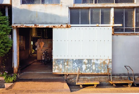 Rust stains mark a pale industrial facade with an open doorway and two low wheeled carts.