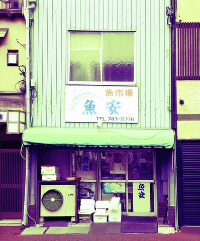 A pale green storefront has a fish-market sign above an air conditioner and stacked boxes.
