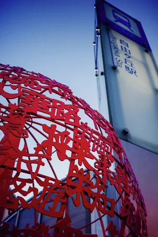 A spherical red framework of Japanese characters rises beside a tall pale sign against blue sky.