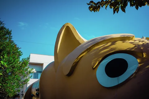 A giant yellow animal head with a large blue-rimmed eye fills the foreground beneath turquoise sky.