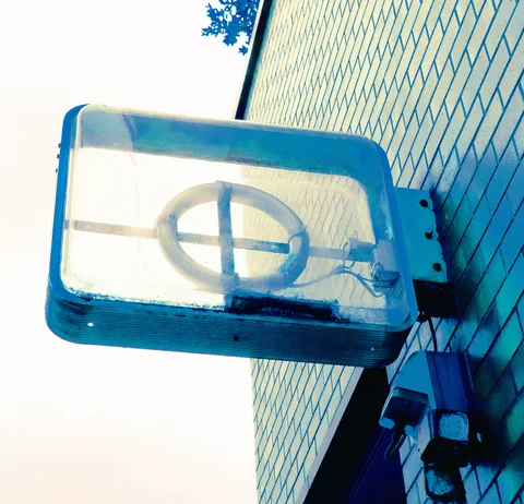 A cracked rectangular projecting sign with a circular symbol hangs beside a blue tiled wall.