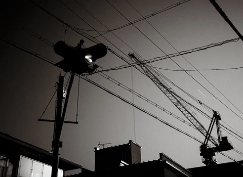 Loudspeakers and a construction crane silhouette beneath a web of overhead wires in monochrome.
