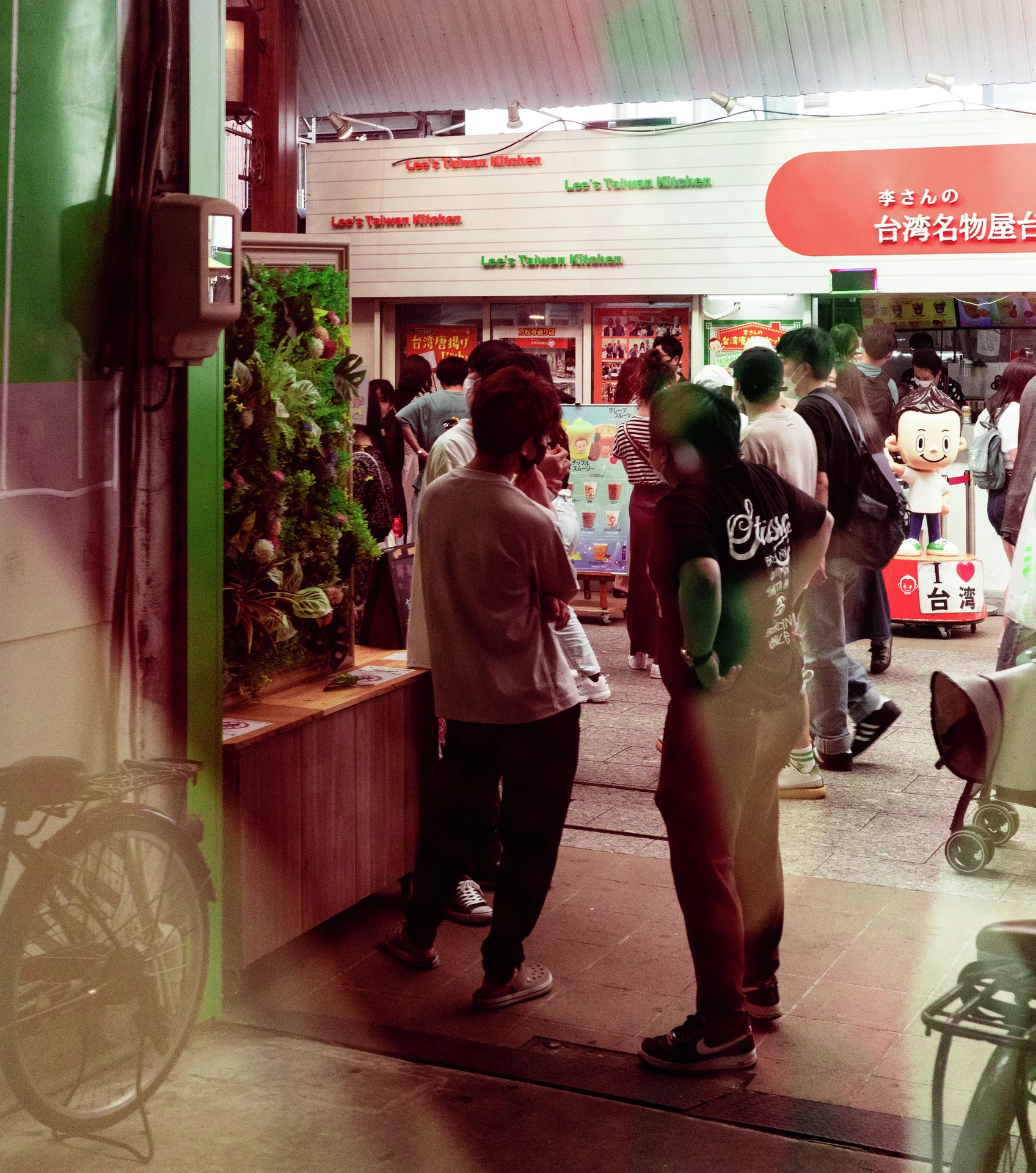 People stand at a brightly lit shop entrance surrounded by posters, merchandise, and bicycles near the doorway.