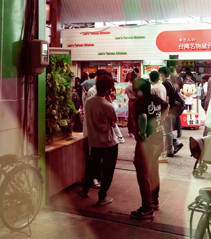People stand at a brightly lit shop entrance surrounded by posters, merchandise, and bicycles near the doorway.