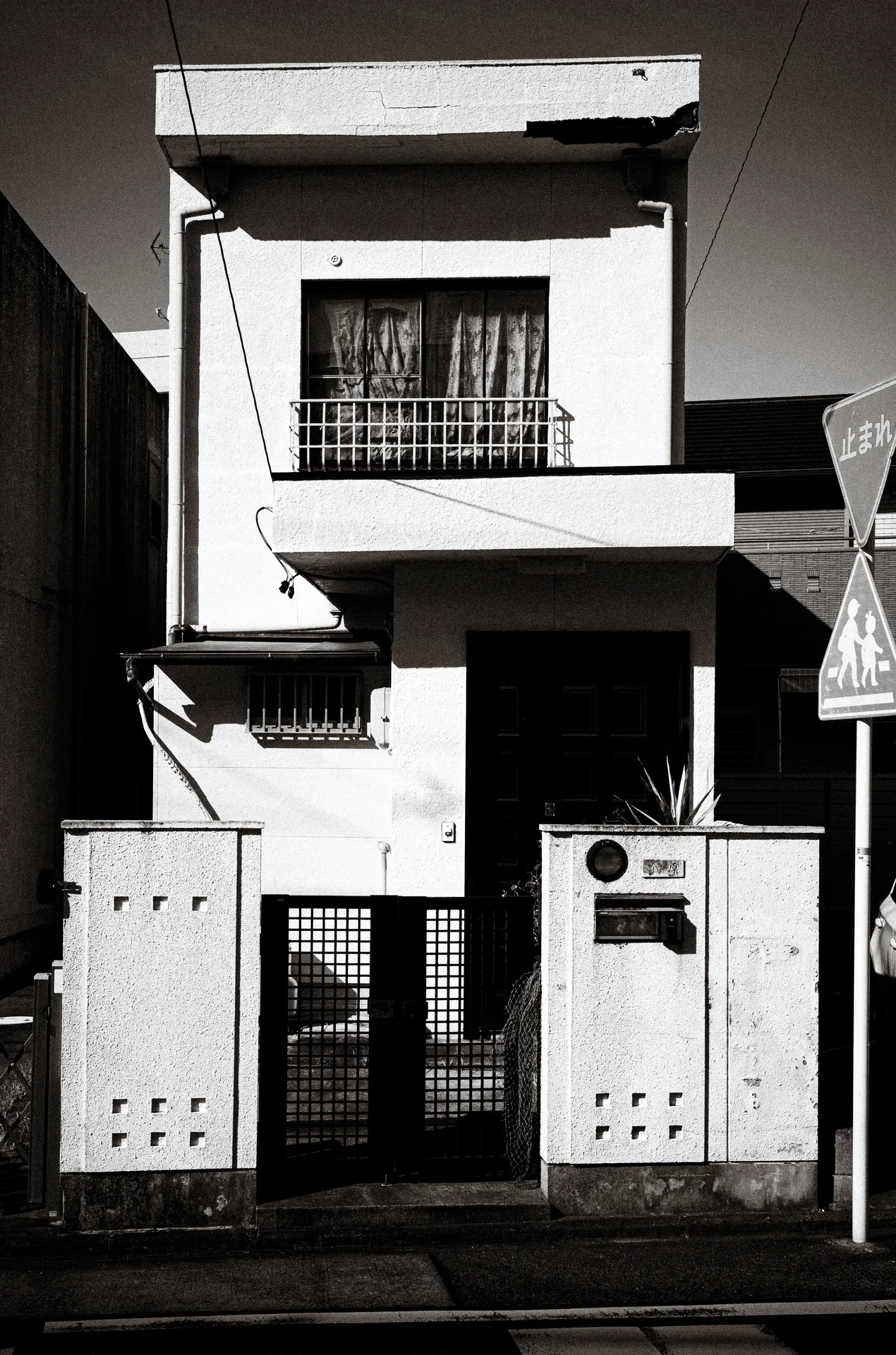 A narrow white house has a small upper balcony above a recessed entrance and metal gate.