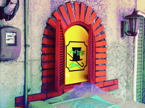 A yellow arched window with an emblem is framed by red bricks beside an old wall lantern.