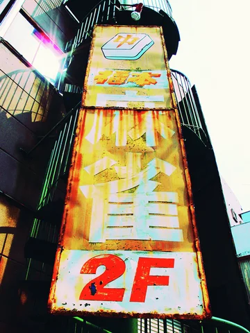 A heavily rusted vertical sign with a red 2F hangs beside a curving outdoor staircase.