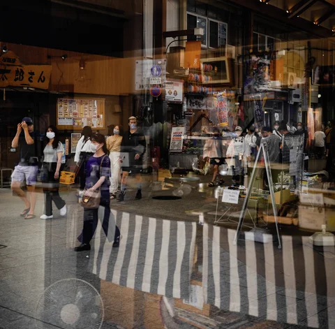 Pedestrians and shop entrances overlap in a glass reflection above a striped panel.