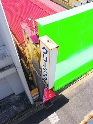 A vivid green awning and vertical Japanese sign project over a narrow street beside a red roof.