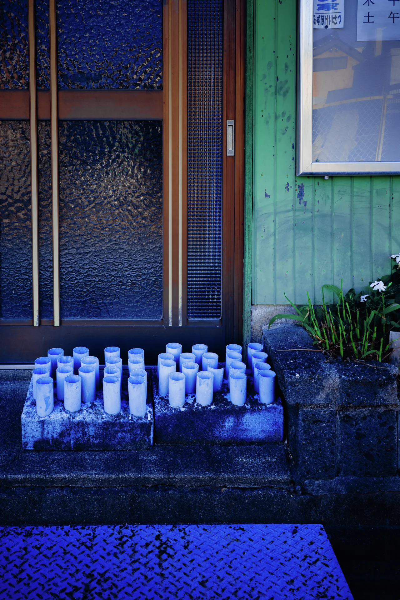 Rows of small white containers line concrete steps outside a green wooden doorway.