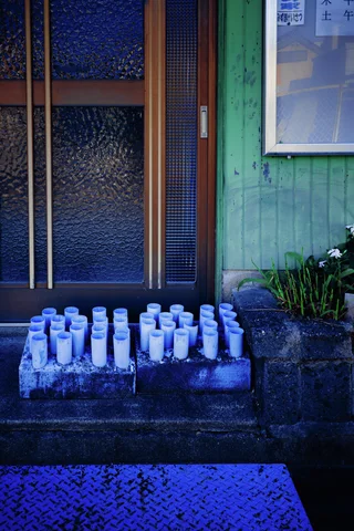 Rows of small white containers line concrete steps outside a green wooden doorway.