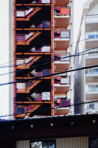 An orange exterior staircase zigzags up a tall apartment building behind crossing utility wires.