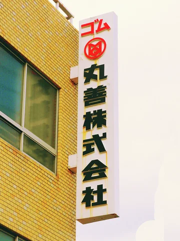 A tall white Japanese sign with a red emblem projects beside yellow brickwork and a broad window.