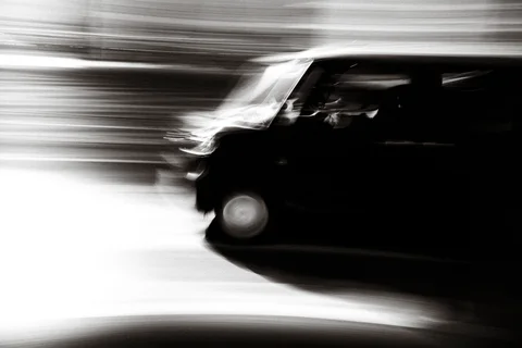 A dark van appears against a streaked bright street background in black and white.