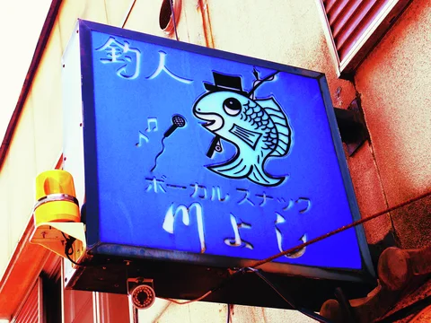 A blue projecting sign shows a cartoon fish wearing a top hat beside a microphone.
