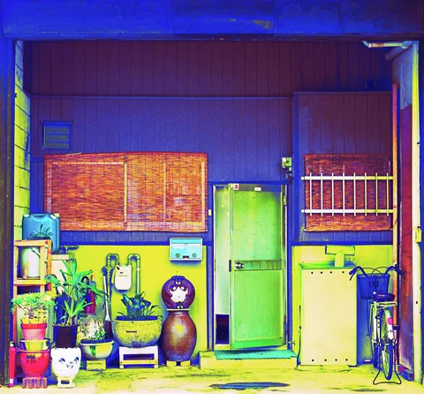 A green door sits between shuttered windows and potted plants on a vivid blue-and-yellow facade.
