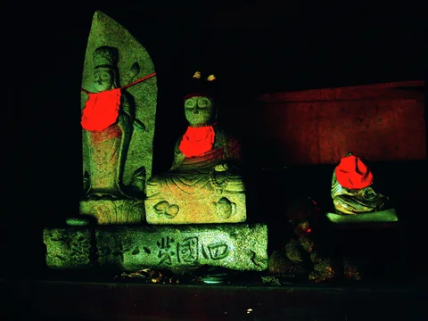 Three stone religious figures wear bright red cloths against a dark wooden background.