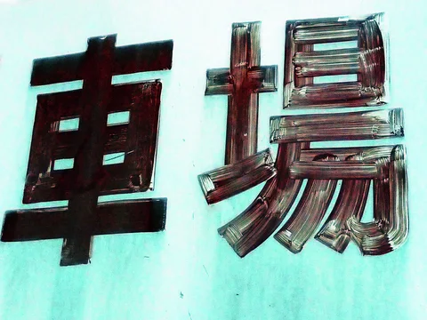 Two large raised metallic characters cast dark shadows on a pale blue wall.