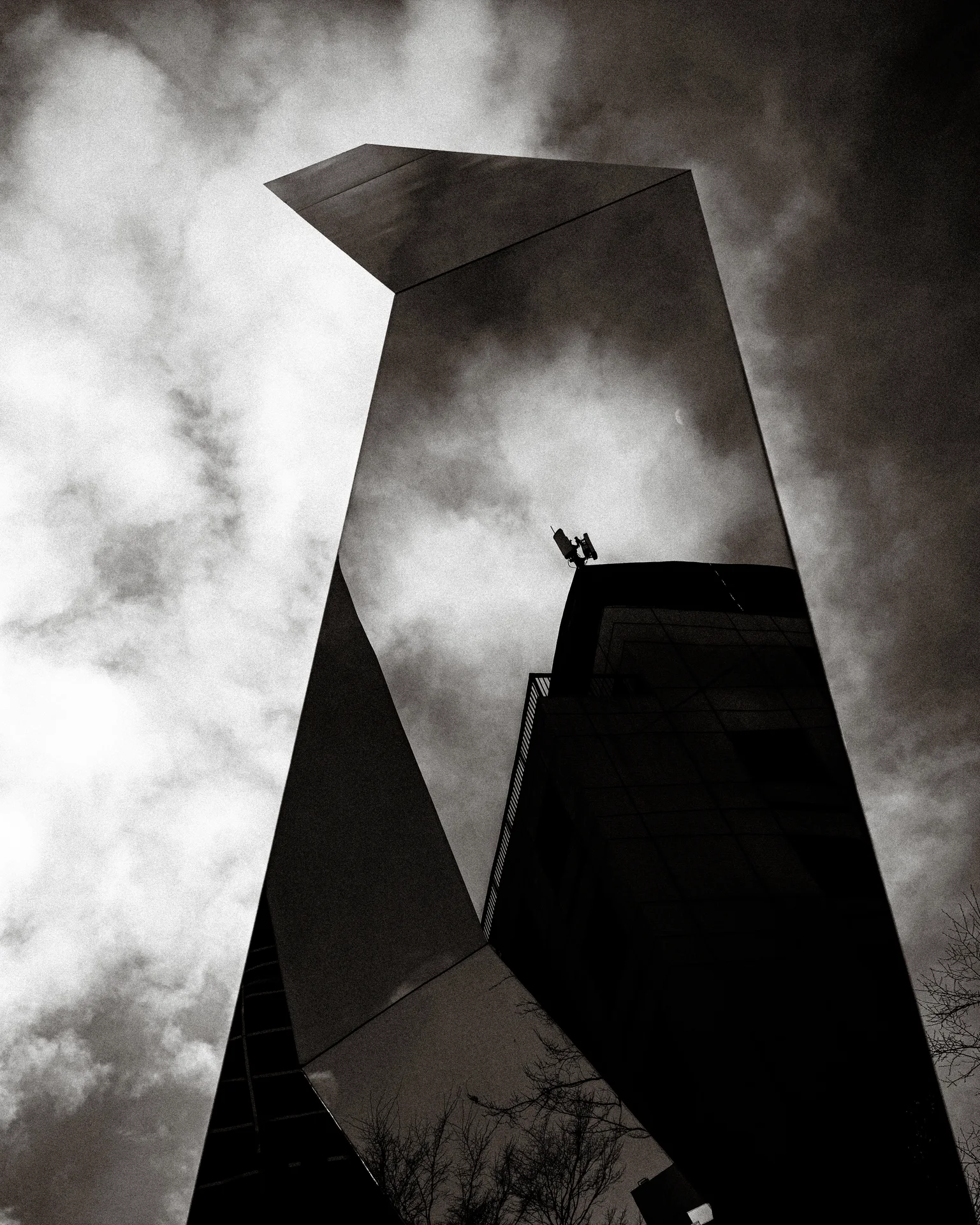 Angular mirrored surfaces reflect cloudy sky and a dark building silhouette in black and white.