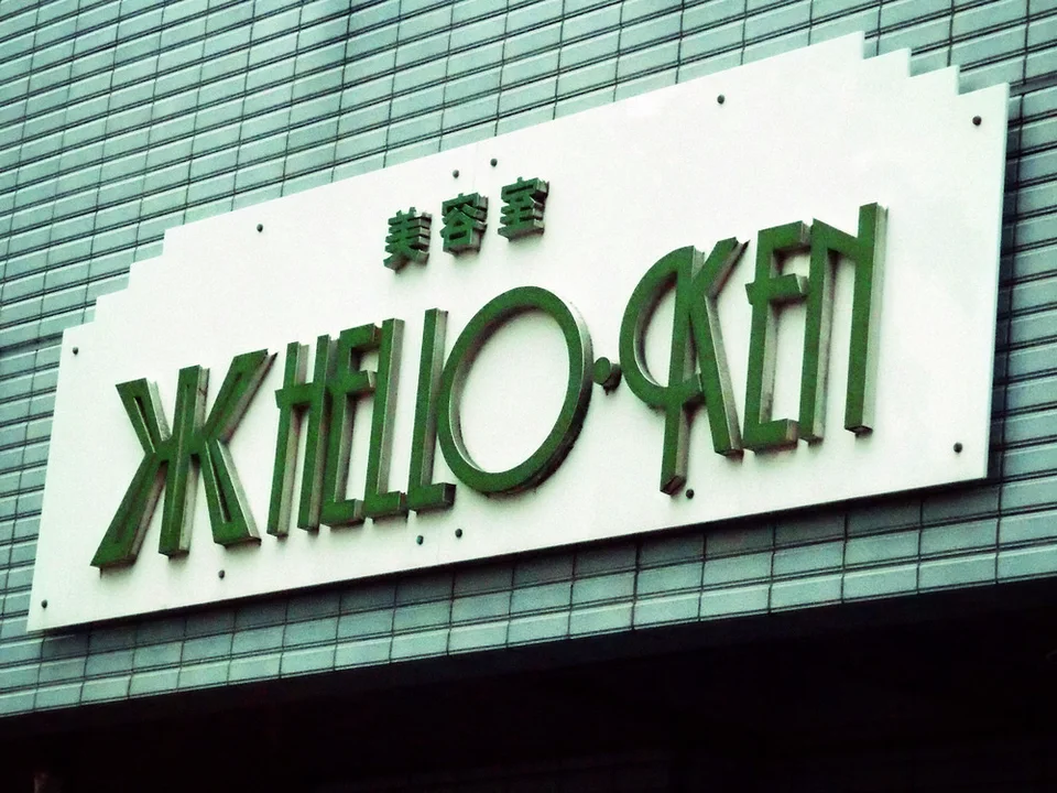 Raised green salon lettering spans a pale rectangular sign mounted on small blue wall tiles.