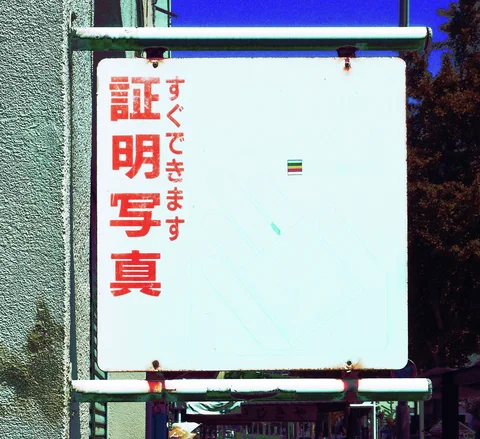 Red Japanese lettering occupies one side of a mostly blank pale sign within rust-stained metal supports.