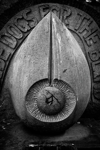 A carved pointed oval ornament with a circular center rests against inscribed stone in black and white.