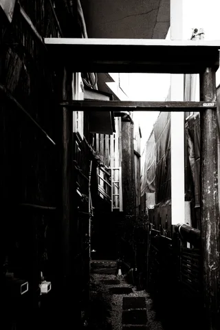 Heavy horizontal beams span a narrow shadowy passage between buildings in black and white.