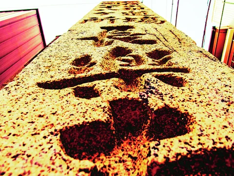 Deeply carved Japanese characters run up a rough stone pillar seen from a steep low angle.
