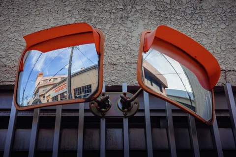Two orange-framed convex mirrors reflect nearby buildings and wires above a barred window.