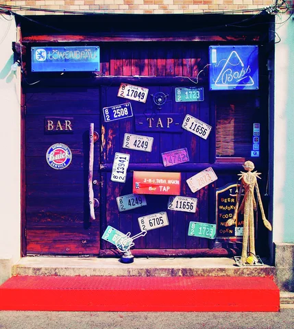 License plates and bar signs decorate a dark entrance above a vivid red step.